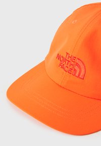 Kollane pesapalli kübar, mis on valmistatud pehmest kangast ja millel on punane tikitud logo. Külg on ümar ja sellel on nähtavad õmblusdetailid.