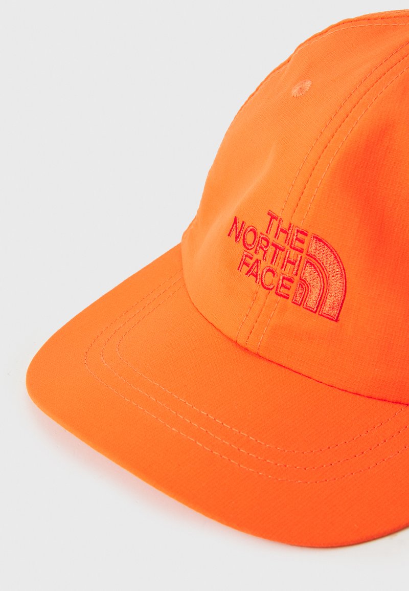 Gorra de béisbol naranja hecha de tela suave, con un logo bordado en rojo. La visera es redondeada y tiene detalles de costura visibles.