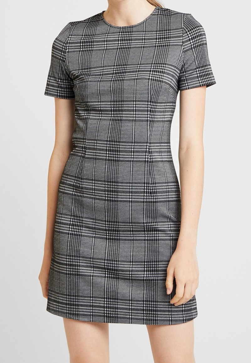 Robe ajustée à manches courtes avec un motif à carreaux noir et blanc. Tissu lisse avec une légère brillance, encolure ronde et silhouette cintrée.