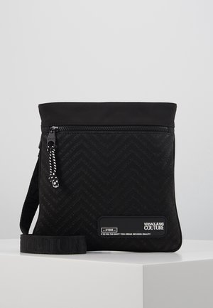 Sac bandoulière noir avec texture chevron, poche avant zippée, sangle de marque et patch logo Versace Jeans Couture.