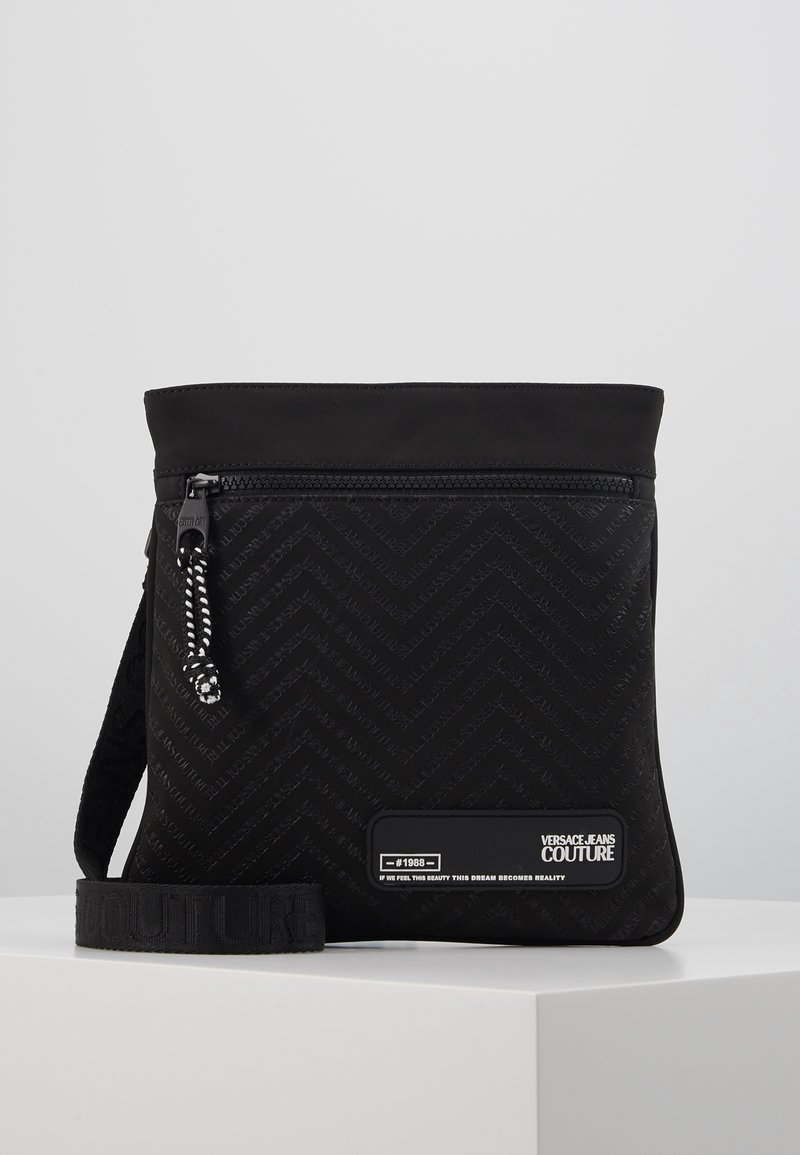 Sort crossbody taske med chevron tekstur, front lynlås lomme, mærket rem og Versace Jeans Couture logo patch.