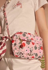 Lyserød blomster crossbody taske med en lynlås-lomme, guldfarvet hardware og en charme formet som et rødt kirsebær. Stoffet har en tekstureret overflade.