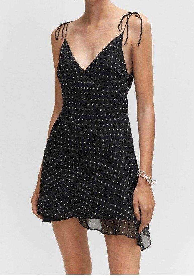 Robe noire sans manches avec un décolleté en V, ornée de pois blancs, avec des bretelles ajustables à nouer et un ourlet asymétrique en tissu léger.