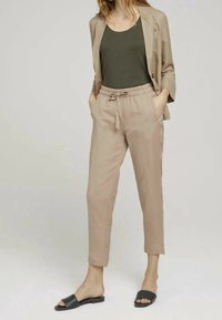 Pantalons beiges ajustés avec une taille élastique et un cordon de serrage. Associés à un débardeur vert foncé et des sandales noires à enfiler. Texture de tissu légère.