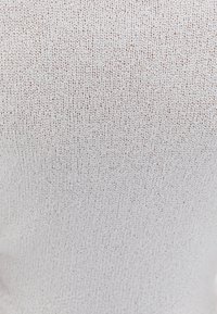 Světlý béžový pletený látkový materiál s jemnou texturou. V celém povrchu jsou jemné tečky, které vytvářejí jednotný vzor. Elastický a příjemný na dotek.