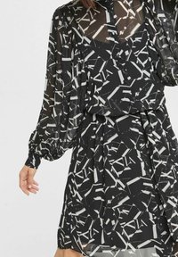 Schwarzes Kleid mit einem transparenten, gemusterten Stoff und weißen abstrakten Designs. Lange, voluminöse Ärmel und eine taillierte Taille.