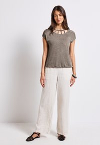 Khaki top s krátkým rukávem a výřezem u krku, v kombinaci s volnými, světlými lněnými kalhotami a černými plochými botami.