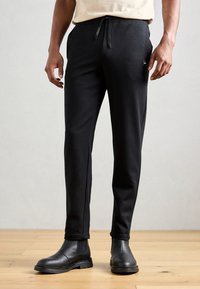 Black sweatpants with a drawstring waist and side pockets. Smooth texture, tailored fit, paired with black ankle boots.