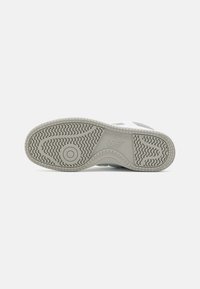Shoe sole featuring a textured gray rubber with a patterned tread, includes a circular accent and embossed branding along the side.