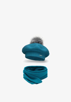 Beret tricotat verde-albastru cu un pompon din blană gri în vârf, asociat cu o eșarfă tricotată asortată. Ambele articole au o textură elegantă și netedă.