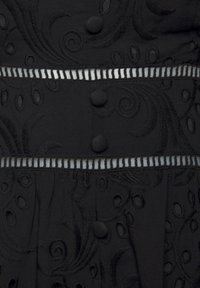 Schwarzer Stoff mit strukturierter Stickerei in gewundenen Mustern; enthält runde Knöpfe und horizontale gestreifte Akzente.