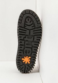 Suela de zapato de goma negra con patrones texturizados, destacando un acento de estrella naranja. Suela diseñada para ofrecer tracción y durabilidad.