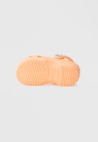 Oranžas gumijas sandales ar teksturētu zoli un apaļu pogas aizdari. Aprīkotas ar caurumiem ventilācijai.