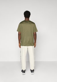Oliven grøn kortærmet t-shirt lavet af glat stof, parret med hvide sweatpants med sorte sidelinjer og atletiske sko.