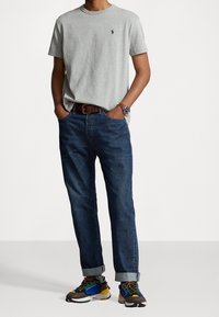 Šedé bavlněné tričko, modré džíny, hnědý opasek, barevné tenisky s různými akcenty. Jednoduchý design, volný střih, krátké rukávy.