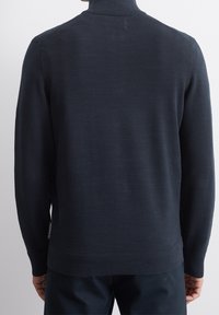 Mörk marinblå stickad tröja med hög krage, ribbade manschetter och texturerat mönster. Har en liten etikett på den nedre sidan.