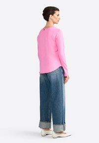 Camicia rosa a maniche lunghe con scollo tondo e dettaglio dei bottoni sul retro, abbinata a jeans in denim blu a gamba larga e scarpe bianche.