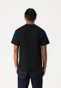 Zwarte katoen T-shirt met korte mouwen, ronde hals en een relaxte pasvorm, gedragen met donkerdenim jeans met stiksels op de achterzak.
