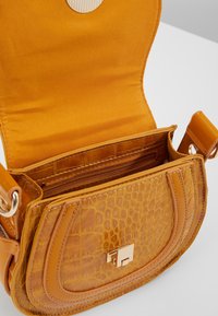 Borsa a spalla in pelle marrone con motivo coccodrillo e chiusura dorata, aletta aperta che rivela una tasca interna con zip e foderatura in tessuto.
