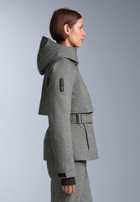 Sivý kabát v herringbone vzore s kapucňou, skrátený strih, široké klopy, opasok v páse a čierne manžety. Obsahuje detail bočnej vrecka.