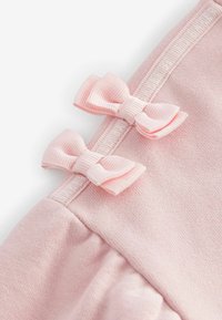 Rosa Stoff mit weicher Textur, der zwei kleine, passende rosa Schleifen am Rand hat. Das Design umfasst eine smockierte Verzierungen.