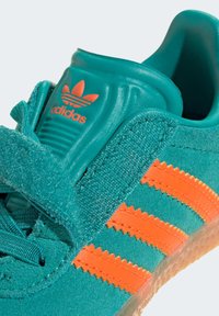 Teal sneakers med orange zigzag-ränder, texturerad ovandel, vadderad tunga och gummisula. Har Adidas-logotyp på tungan.