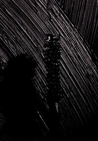 Czarna teksturowana powierzchnia z pionowymi pociągnięciami pędzla i centralnym cylindrycznym elementem. Tekstura wydaje się gładka obok wypukłych wzorów.