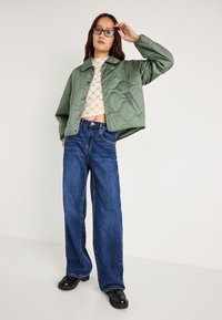 Κουρελού πράσινο μπουφάν, ελαφρύ, με κοντή σχεδίαση. Συνδυάζεται με ψηλοκάβαλο φαρδύ τζιν σε μπλε απόχρωση και μαύρα παπούτσια. Τα γυαλιά συμπληρώνουν την εμφάνιση.