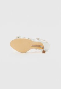 White high-heeled sandal with a metallic sheen. Features slender straps and a beige sole with blue accent lines. Smooth texture.