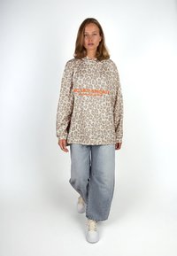 Leopard-print beige hooded sweatshirt with orange text detail, paired with light blue wide-leg jeans and white sneakers.