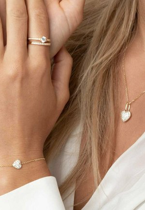 Guld-temat smyckeset med ett hjärtformad hängsmycke och matchande armband. Delarna har glittrande detaljer och lätta kedjor.