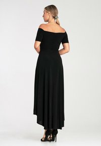 Czarna sukienka na ramiączkach z dopasowaną górą i zwiewnym dołem, z wysokim przodem i niskim tyłem oraz gładką fakturą. Czarne szpilki.
