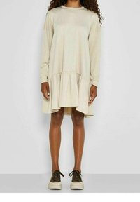 Beige šaty s dlouhým rukávem a rozšířeným lemem, vyrobené z měkké látky. Spárované s hnědými teniskami s robustní podrážkou.