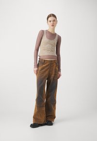 Débardeur beige avec un motif subtil, associé à un pantalon en velours côtelé marron évasé avec une fermeture à boutons et une surface texturée. Chaussures à plateforme noires.