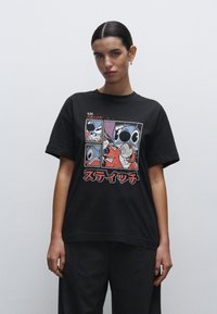 Sort bomulds T-shirt med et grafisk print af animerede figurer. Korte ærmer, afslappet pasform og bemærkelsesværdig japansk tekst i rød.