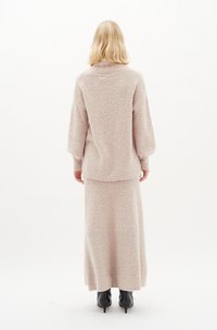 Maglione lavorato a maglia di un delicato rosa con vestibilità rilassata e maniche lunghe, abbinato a una gonna lunga fino alla caviglia dello stesso colore. Stivali neri con tacco alto completano l'outfit.