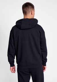 Svart hoodie med en rymlig huva, långa ärmar, ribbade mudd och nederdel. Tillverkad av mjukt material och har en minimalistisk design utan mönster.