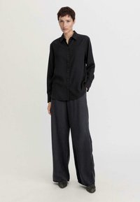 Black, button-up shirt made of smooth fabric, paired with loose, dark gray wide-leg trousers, featuring a relaxed fit.