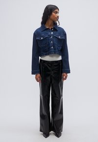 Κοντό τζιν μπουφάν με ασημένια κουμπιά και δύο τσέπες στο στήθος. Συνδυάζεται με ψηλόμεσο μαύρο ψεύτικο δερμάτινο παντελόνι με φαρδιά ποδάρια.