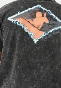 Camiseta gráfica negra de tejido suave con una estampado colorido en forma de diamante de una escena de surf en naranja y azul en la parte de atrás.