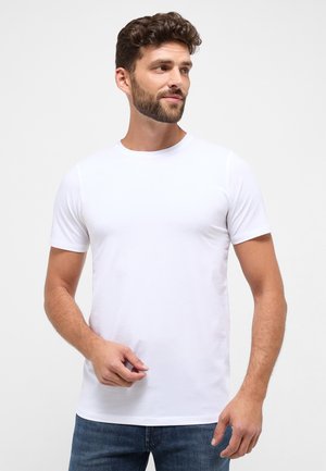 T-shirt bianca a maniche corte realizzata in tessuto morbido, con colletto rotondo e un design aderente, abbinata a jeans blu scuro.