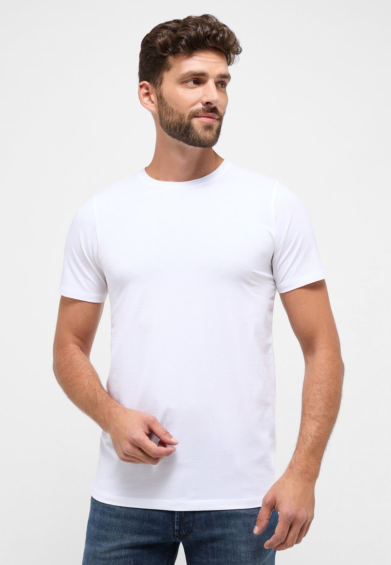 Hvid kortærmet t-shirt lavet af blødt stof, med rund hals og en tætsiddende pasform, parret med mørkeblå jeans.