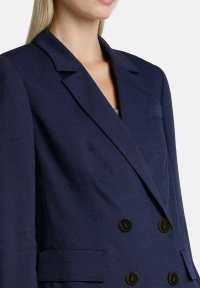 Navy blue double-breasted blazer with a textured finish, notch lapel, and two front pockets; features gold-tone buttons and structured shape.