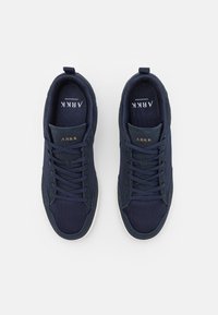 Námořnické modré sportovní boty s texturou síťoviny a semiše, šněrovací design, kontrastní bílá podešev a zlaté logo na jazyku.