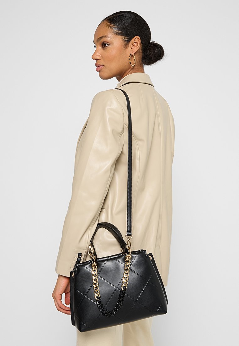 Sac à main noir avec un design matelassé, doté d'une anse accentuée par une chaîne et d'une bandoulière amovible, fabriqué en cuir lisse.