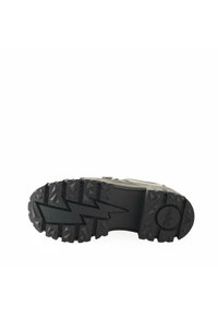 Suela de zapato de goma negra con patrones de tracción profundos, que presenta un diseño en zigzag y un detalle de logo circular en el talón.