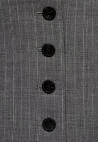 Tela gris con rayas verticales, que presenta cuatro grandes botones negros en el frente. Textura suave con un ligero brillo.