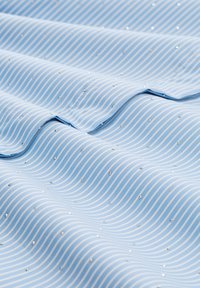 Light blue fabric with white wavy stripes and small shiny embellishments evenly spaced across the texture, creating a soft, smooth appearance.