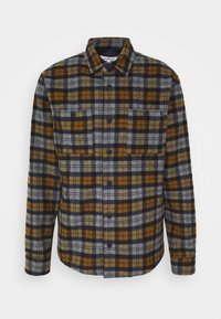 Flannel shirt featuring a plaid pattern in dark blue, mustard yellow, and gray tones. It has a button-up front and two chest pockets.