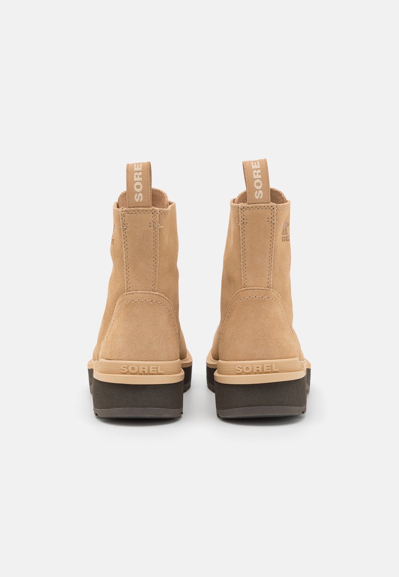 Suede-Stiefeletten in hellbraun mit einer schwarzen Gummisohle. Merkmale sind auffällige Zuglaschen an der Rückseite und ein geprägtes Markenlogo an der Ferse.